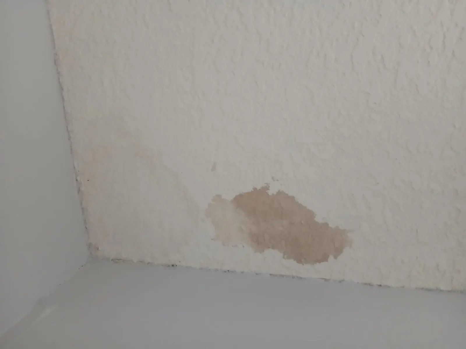 Textured ceiling corner with a brown stain before the repaint